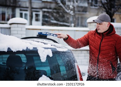 Man Cleaning Car From Snow And Ice With Brush And Scraper Tool During Snowfall. Winter Emergency. Weather-related Vehicle Emergencies. Automobile Covered With Snow