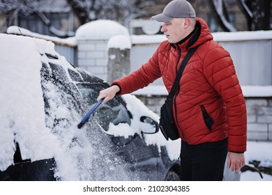 Man Cleaning Car From Snow And Ice With Brush And Scraper Tool During Snowfall. Winter Emergency. Weather-related Vehicle Emergencies. Automobile Covered With Snow