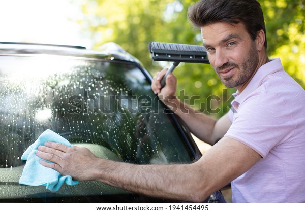 man cleaning car\
windshield with cloth