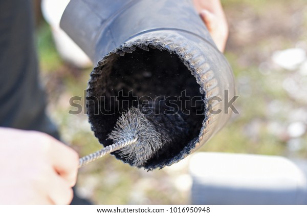 Man cleaning chimney pipe outside.\
Cleaning a wood burning stove. Chimney sweep\
cleaning