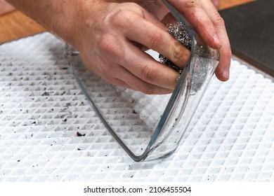 A man is cleaning a dirty baking dish with a thick layer of carbon with an iron washcloth. Glassware for baking with soot, carbon deposits, old dried fat.