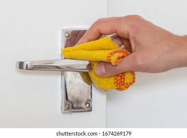 Man Cleaning A Door Knob. Cleaning A Silver Handle With A Yellow Chiffon. Disinfecting To Kill Germs, Viruses And Bacteria