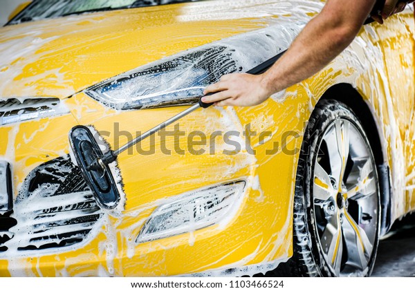 Man cleaning front bumper. Car wash\
using foam and brush. Vehicle wheel detail or close\
up.