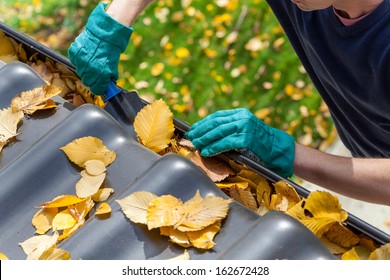 Man cleaning the gutter from autumn leaves