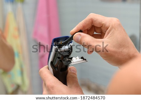 A man cleaning a hair clipper with a brush