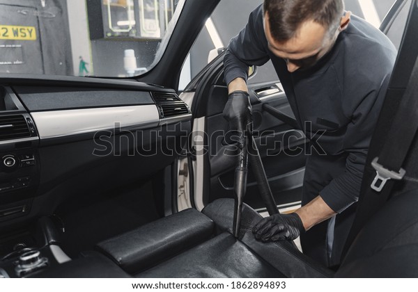 Man cleaning his car with vacuum cleaner. Man in\
a black uniform.