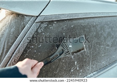 Man is cleaning an icy window on a car with an ice scraper. Cold snowy and frosty morning. Focus on the ice scraper.