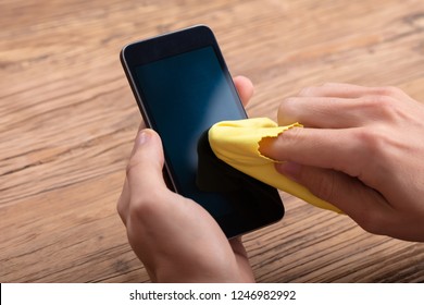 Man Cleaning Mobile Phone Screen With Yellow Cloth Over Wooden Desk - Powered by Shutterstock