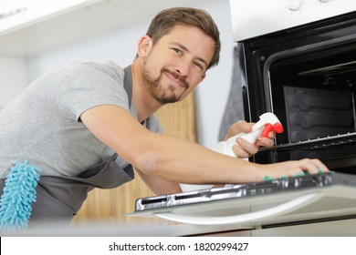 Man Cleaning Oven Door At Home Kitchen