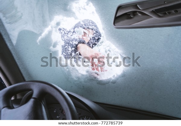 Man cleaning snow from the car front glass. View\
from inside of the vehicle.