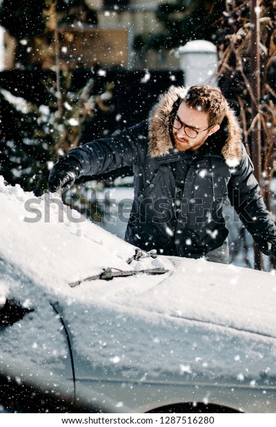 Man cleaning snow from car.\
Transportation and car cleaning during winter\
snowfall