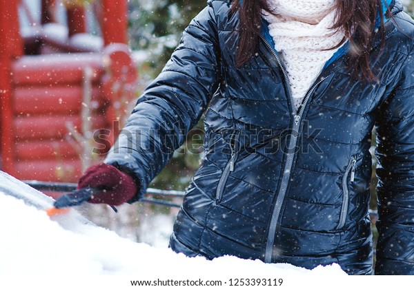 Man cleaning snow from car windshield with brush,\
close up. Woman removing snow from car. Snowy winter weather. Car\
in snow after snowstorm. Transportation, winter, weather and\
vehicle concept