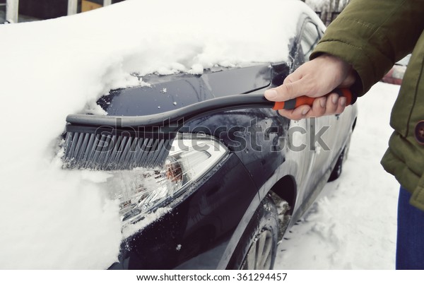 Man cleaning snow from car windshield with\
brush.Removing snow from\
car