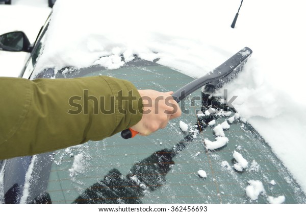 Man cleaning snow from car windshield with\
brush.Removing snow from\
car