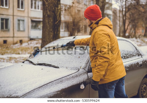 Man cleaning snow from car windshield with
brush.Removing snow from
car