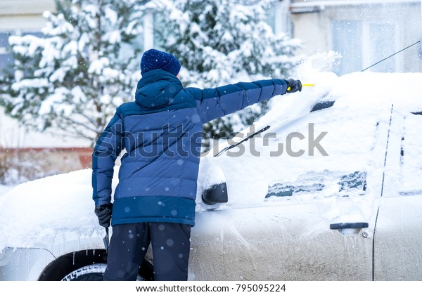 Man cleaning\
snow from car windshield with\
brush
