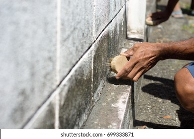 Man Cleaning Stains On Concrete Walls With A Brass Wire Brush In Hand