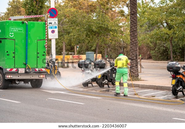 Man\
cleaning streets in Barcelona with water hose and municipal\
vehicle. Barcelona, Spain - September 14,\
2022.