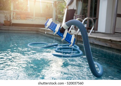 Man cleaning swimming pool with vacuum tube cleaner early in the morning