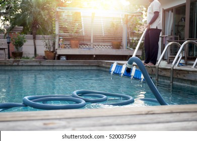 Man Cleaning Swimming Pool With Vacuum Tube Cleaner Early In The Morning