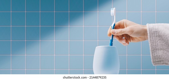 Man cleaning teeth in the bathroom, he is taking his toothbrush in the toothbrush holder - Powered by Shutterstock