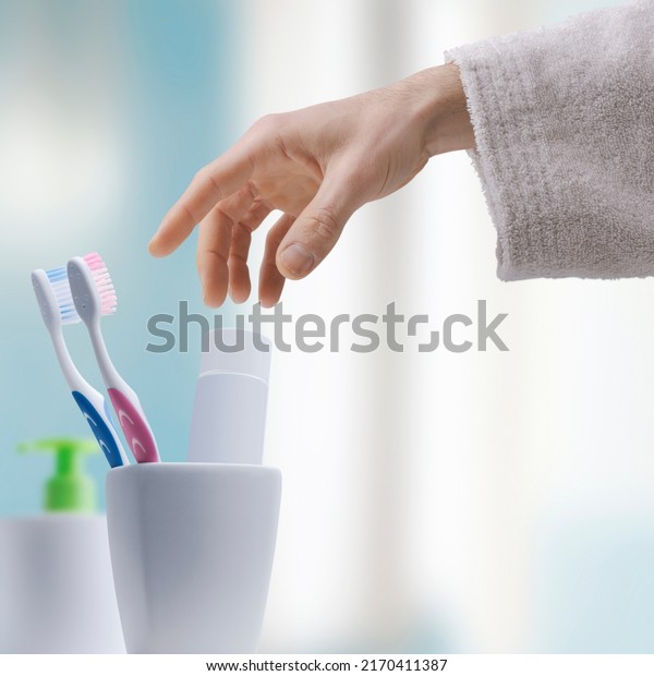 Man cleaning teeth in the bathroom, he\
is taking his toothbrush in the toothbrush\
holder