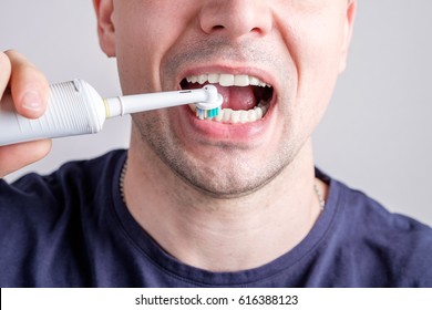 man cleaning teeth with electric toothbrush closeup