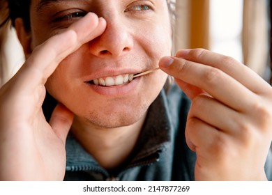 Man Cleaning teeth with a toothpick hiding mouth with hand. Male using Disposable Double-end Teeth Stick Floss Pick to clean teeth. Toothpick Dental Brush Oral Care concept