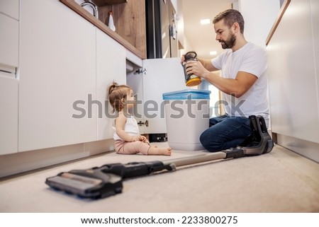 A man is cleaning vacuum cleaner while his baby is looking at him.