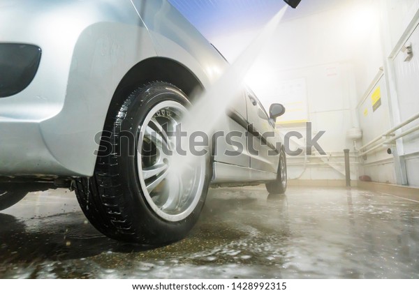 Man cleaning vehicle with high pressure water spray\
or jet. Car wash details. wash the wheels with water. washing the\
rear wheel of a car