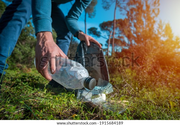 Man cleaning-up the forest of plastic garbage.\
Nature cleaning. Volunteer picking up a plastic bottle in the\
woods. Green and clean nature. Plastic awareness activism and\
ecology concept