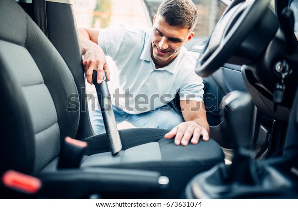 Man cleans car\
interior with vacuum\
cleaner