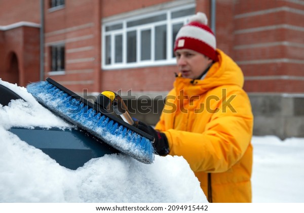 A man cleans the car from snow with a brush.\
Climate, weather.