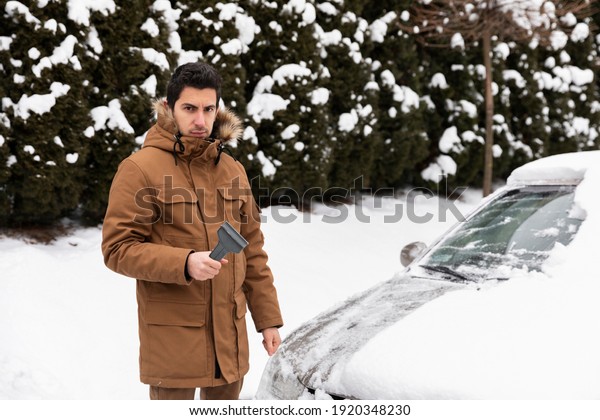 The man cleans the car of\
snow and ice. The guy is not happy with the choice of snow removal\
tool.