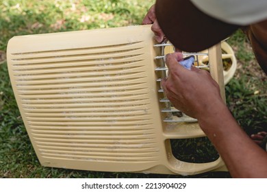 A Man Cleans The Front Grille Of A Window Type Air Conditioner With A Washrag And Soap Outside. Aircon Cleaning Service.