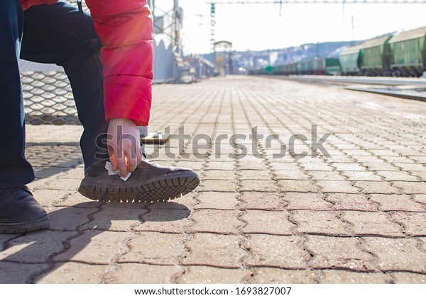 a man cleans shoes, boots with a\
wet cloth, a rag, while on the platform of a railway station\
against the background of rails, tracks and freight\
cars