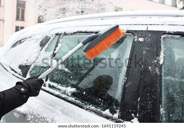 Man cleans the snow from a car with a brush. Winter
car care.