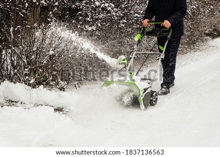 Man cleans snow off path with wireless electric snow blower
