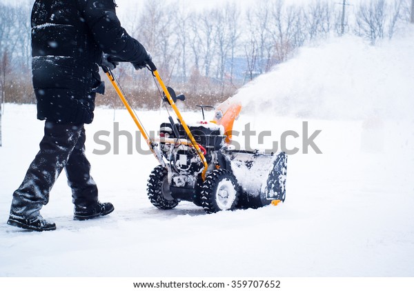 A man\
cleans snow from sidewalks with\
snowblower.