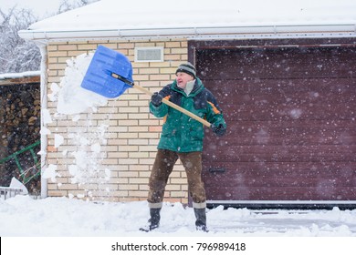 A Man Cleans Snow In Winter Weather With A Shovel Near The Garage