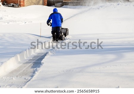 Man clearing a path using a snow blower to clear a residential driveway after a snowfall