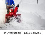 Man clearing or removing snow with a snowblower on snowy road detail.
