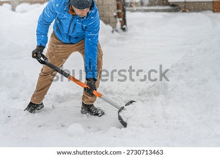 Man clearing snow from a driveway using a snow shovel. Winter sidewalks maintenance.