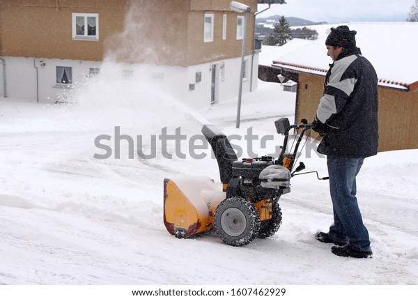 A\
man clears the road and the sidewalk with a snow\
blower