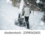 A man clears the snow from the street with a powerful snowblower after a heavy winter storm. Using a snowblower machine, a man works to remove the snowdrifts from the sidewalk in a snowy city.