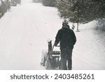 A man clears the snow from the street with a powerful snowblower after a heavy winter storm. Using a snowblower machine, a man works to remove the snowdrifts from the sidewalk in a snowy city.
