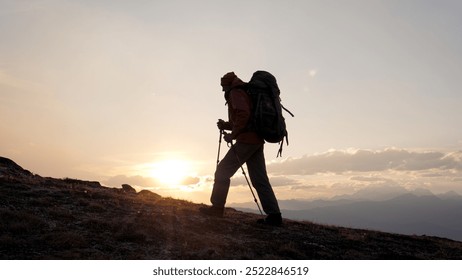 Man climber with backpack and trekking sticks poles raises up to top of cliff mountain. Walking at sunrise or sunset, sun rays shine background. Dressed in warm trekking clothes hiking. Shot in motion - Powered by Shutterstock