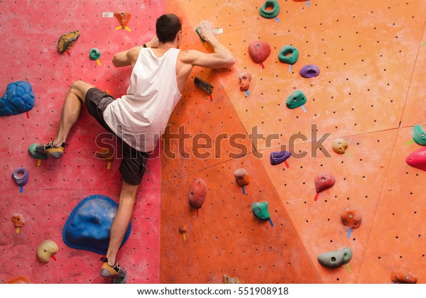 Man\
climber on artificial climbing wall in bouldering\
gym