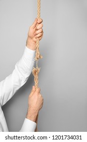 Man Climbing Frayed Rope On Gray Background