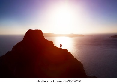 Man climbing up hill to reach the peak of the mountain over ocean. Persistence, determination, strength, reaching the target concepts. 
